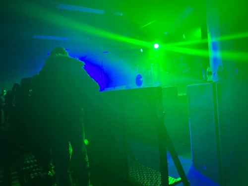 Emma's view at Asylum Main Room in Birmingham. The stage is somewhat visible under green and blue lights with the barrier visible just in front of it.